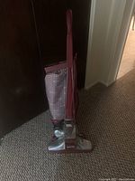 Front view of Kirby Legend II vacuum cleaner upright, showing the red handle, metallic silver base, and patterned cloth vacuum bag.