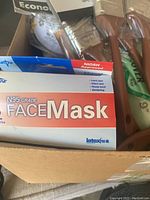 Box containing new N95 grade face masks and multiple paint brushes.