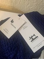 Close-up photo of two tags from the leggings showing branding and logos including QUQOTA and NEW TREND with the text 'GIVE U THE BEST' and a sewing machine icon.