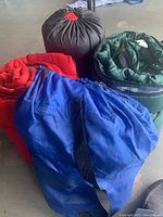 Three sleeping bags in red, green, and blue in their compression sacks, showing different colors and carrying straps.