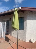 Full view of green outdoor umbrella closed, attached to metal pole and metal base stand placed on patio.