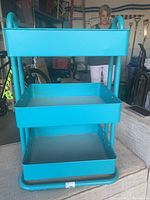 Blue 3-tier metal utility storage rack with open trays and rounded legs in garage setting