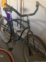 Side view showing black frame with distinctive curved top tube, wide black handlebars, black saddle with spring, white-walled tires, and chain guard.