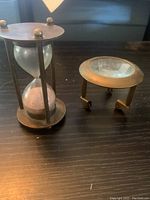 Photo showing a vintage sand hourglass with a brass frame and a brass map reader magnifier with folding legs.
