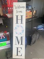 Wooden tall decorative sign standing upright, showing the full design with text and floral wreath.