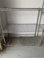 Full view of the metal wire storage rack showing three shelves and four support legs.