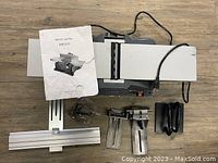 Top-down photo showing bench jointer main body, user manual, aluminum track guide, metal guides, and black plastic attachments spread out on floor.