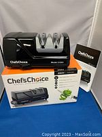 Front view of the Chef's Choice electric knife sharpener on top of the product box with the instruction manual displayed beside it.