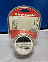 Front view of KitchenAid digital timer in original packaging showing timer face with three control buttons and branding.