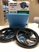 Photo of AB Wheel exerciser wheels, handles, and blue knee pad in front of the packaging box.