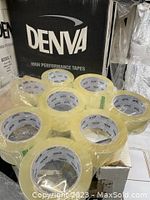 Group of 8 clear packaging tape rolls stacked on a cardboard box with Denva branding in background