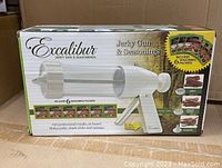 Box front showing Excalibur Jerky Gun & Seasonings branding, capacity 1 lb, includes 6 seasoning packets, picture of jerky, snack sticks, and sausage.