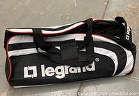 Front side view of the black and white Legrand branded sport duffle bag showing logo, handle and front zippered compartment.