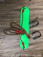 Green plastic swing with brown ropes and two black metal carabiners on wooden floor.