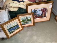 Three framed acrylic paintings displayed on floor, showing landscapes and autumn scene.