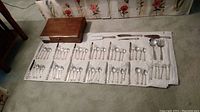 Full set of flatware and accessories laid out on cloth with wooden flatware box visible
