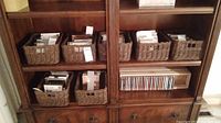 Shelf with six woven baskets filled with CDs and a wooden shelf with CDs lined up vertically in cases