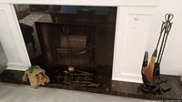 Fireplace with log holder, brass ladle, decorative dog sculpture, and metal fireplace tool stand with broom