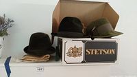 Two hats positioned on a Stetson box, one black with feather, one dark green, both vintage felt style.
