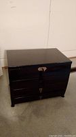 Closed view of black wood jewelry box with three drawers.
