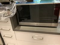 Panasonic Genius Prestige Plus microwave oven on countertop, front view showing brand and door.