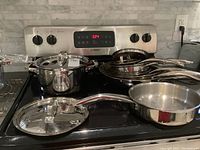 Wide view of set displayed on stovetop showing all fry pans, saucepans and stock pot with lids
