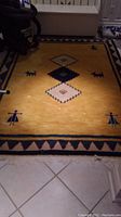 Full view of gold background area rug with central geometric medallions and stylized figures