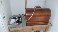 Singer sewing machine case and metal tray with sundries on a worn textile surface.