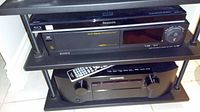 Three stacked electronics units on a rack: Blu-ray player top, stereo middle, receiver bottom