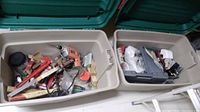 Wide view showing two plastic bins filled with various hand tools, paint supplies, and hardware including levels and wrenches.