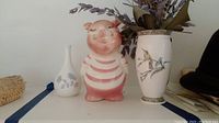 Front view of two vases and a pink ceramic piggy bank with coins inside.