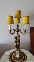 Pair of brass and crystal lamps, each with goddess figure base, four candlestick lights, and yellow velvet shades with gold trim, standing on round carpeted area.