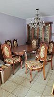Six wooden dining chairs with floral upholstered seats and backs placed around a wooden dining table, visible tiled floor and wall.