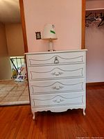 Front view of the white wood dresser showing four drawers with decorative fronts and metal handles