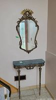 Photo showing vintage cast metal hall table with green marble top and ornate detailed legs below matching intricately framed mirror.