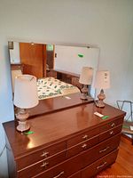 Pair of table lamps placed on a wooden dresser with a large mirror in background, showing full lamps and shadows.
