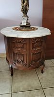 Front view of the side table showing the marble top, carved wooden base, and cabinet doors closed.