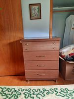 Front view of the MCM wooden dresser with four drawers, brass handles, and wood finish, showing its condition and size in a room corner.