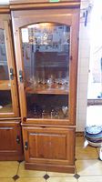Full view of tall wood cabinet with glass door showing storage shelves inside.
