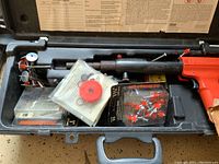 Remington air nailer in a black plastic case with packaging containing nails and red plastic accessories.