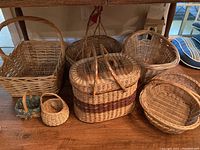 Seven baskets arranged on a wooden surface showing different shapes and sizes, including handled and open-top baskets.
