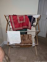 Wooden drying rack with various textiles draped including pillow covers, blankets, and tablecloth.