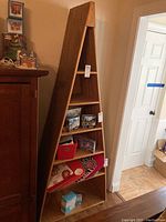 Front view of the canoe-shaped wooden bookcase loaded with a few items on shelves. Shows triangular design and shelf spacing.