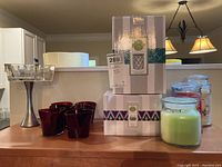 Photo of six red votive cups, two boxed Scentsy wax melts, and one clear glass footed candy dish on a wooden surface.