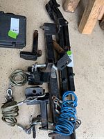 Photo showing black metal tow hitch parts, blue coiled tow cables, steel wire cables, and mounting brackets laid on garage floor