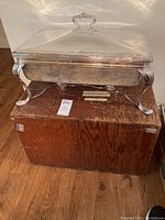 Front and top view of the silver plated chafing dish with ornate legs and lid handle, sitting on top of the wooden storage box.