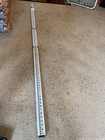 Full view of the collapsed aluminum water depth finder measuring stick on the floor, showing white body with black and red measurement markings up to 8 feet.
