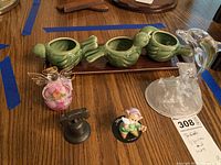 Photo showing all six items: ceramic bird candle holders on tray, glass angel, Liberty Bell replica, glass dolphin, Dopey figurine, and metal bell