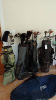 Four golf bags lined up against a wall, filled with golf clubs, showing overall lot contents and condition.