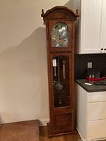 Full view of tall grandfather clock showing wooden body and clock face with glass door below.